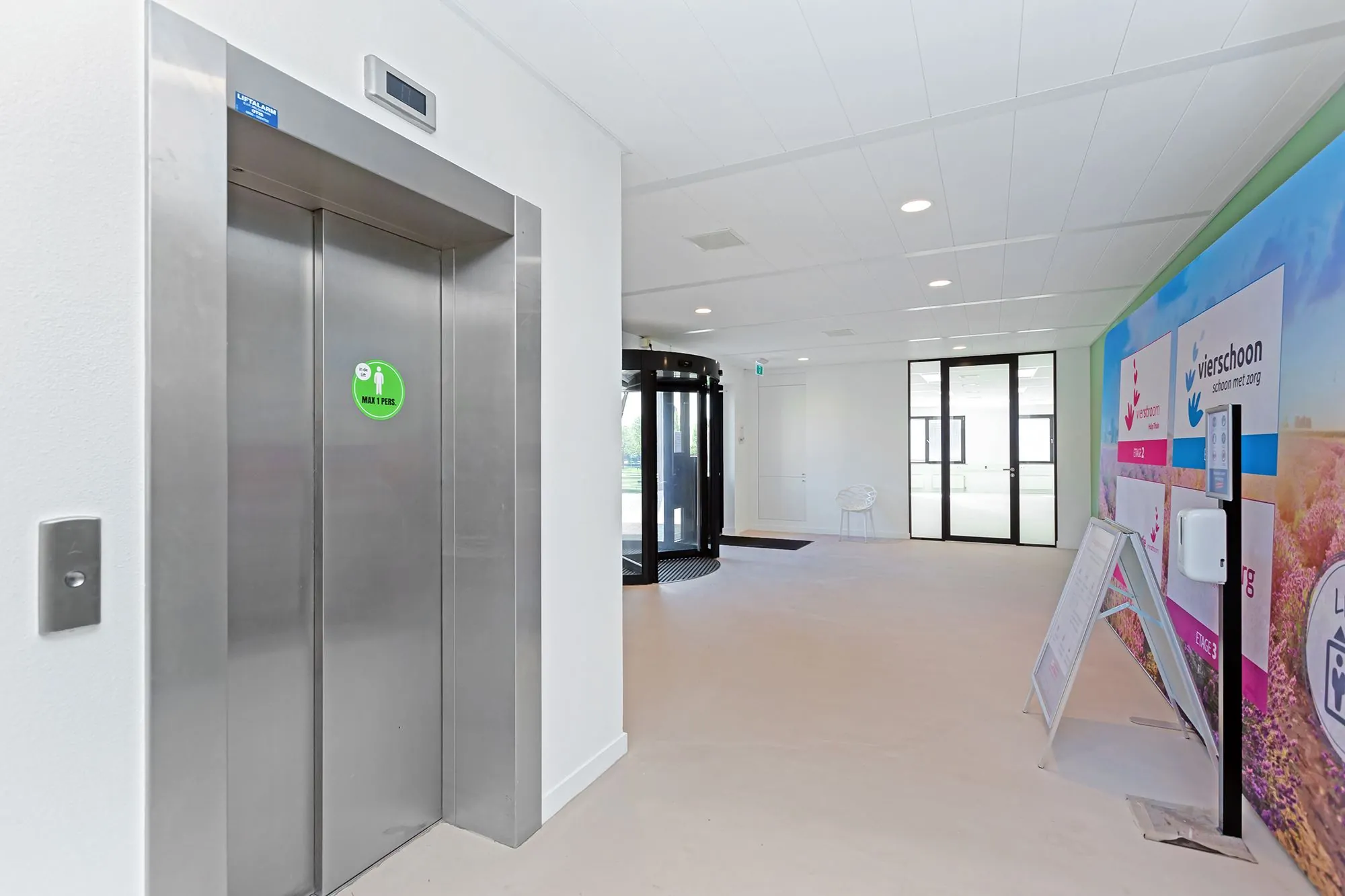 Moderne entreehal met een lift, automatische draaideur en kleurrijke wand met het logo van Vierschoon.